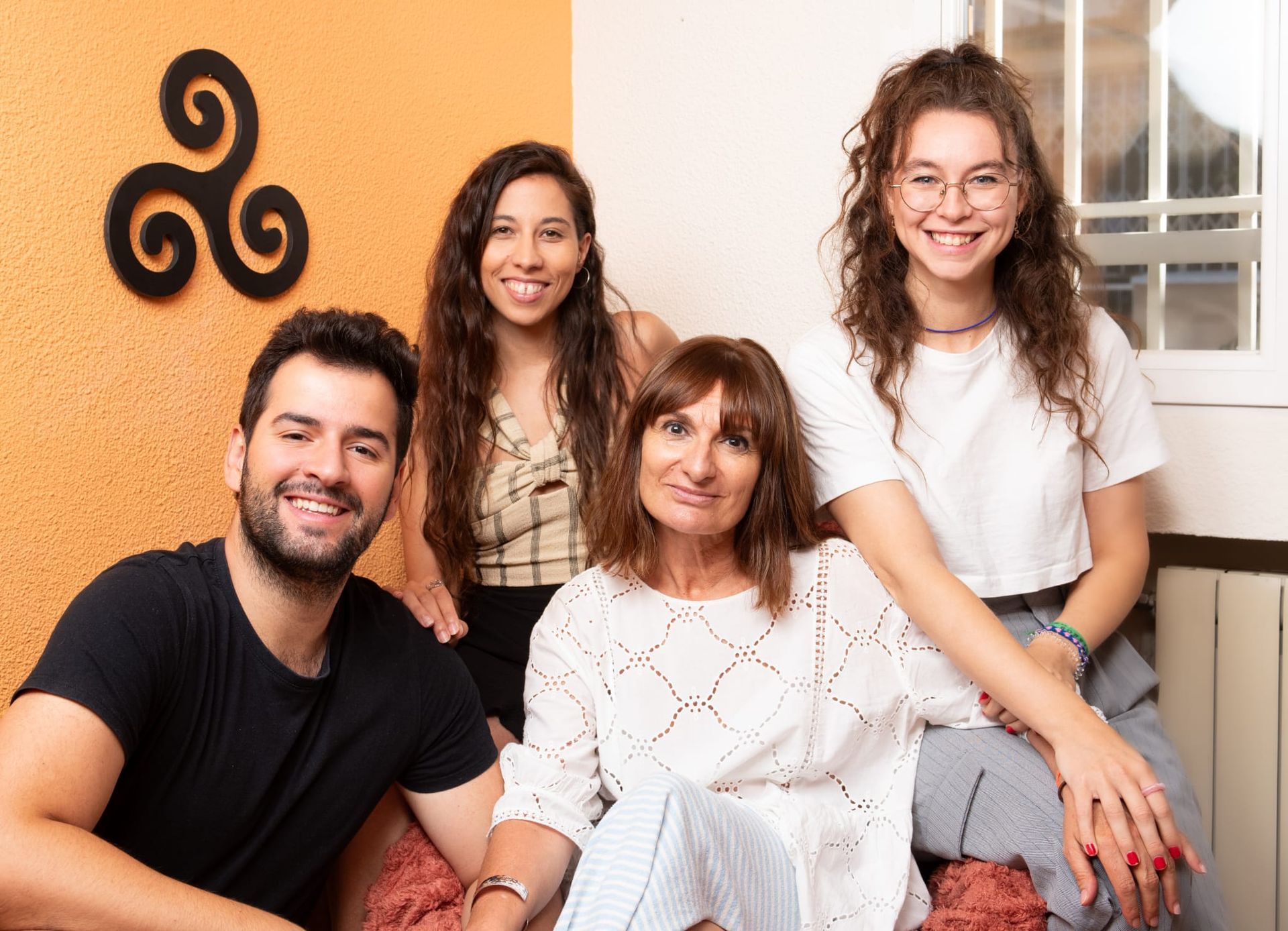 Cuatro personas sonrientes posan juntas: un hombre, dos mujeres y una mujer más joven, en el interior.