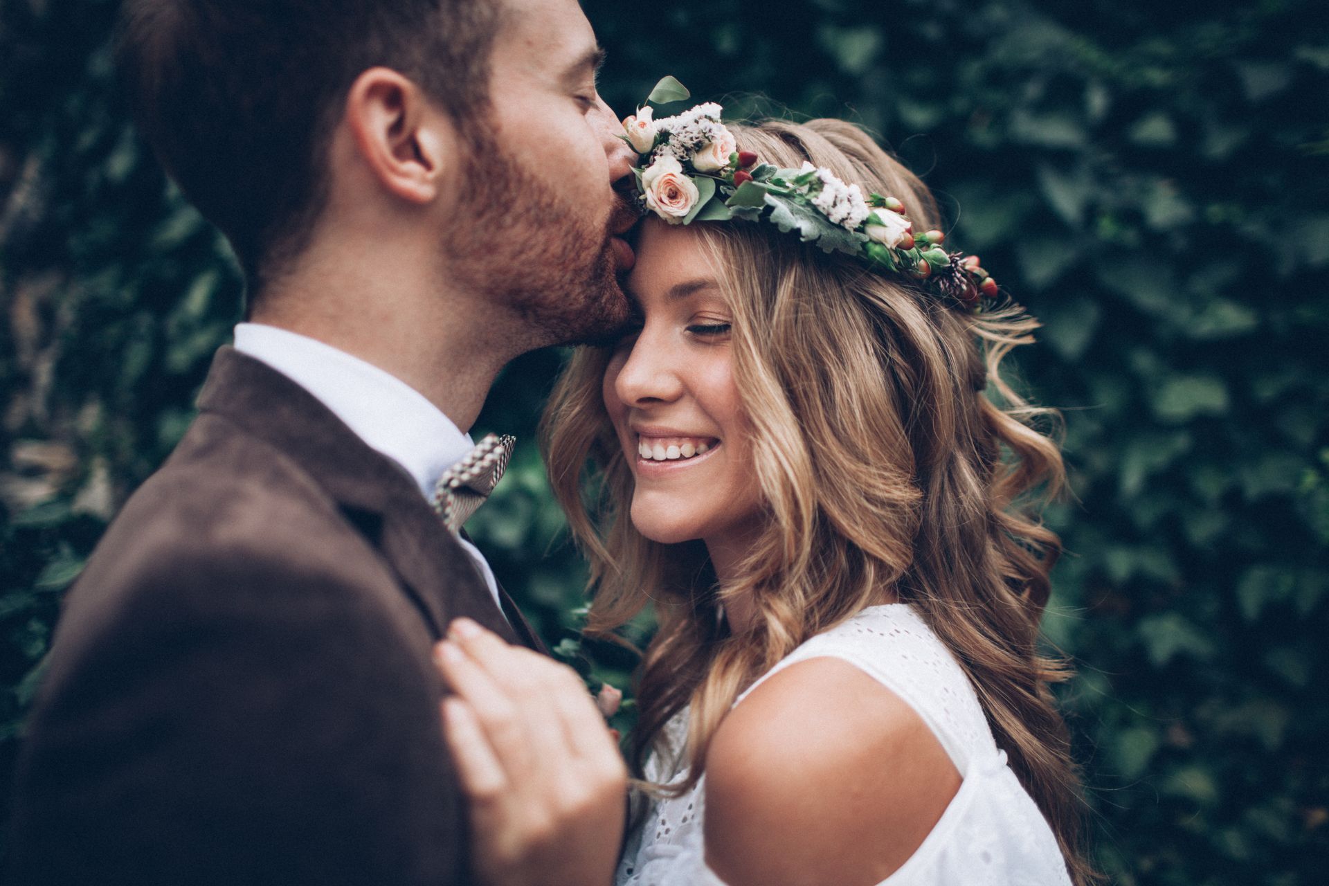 Un couple s'embrasse en plein air ; l'homme embrasse une femme souriante portant une couronne de fleurs.