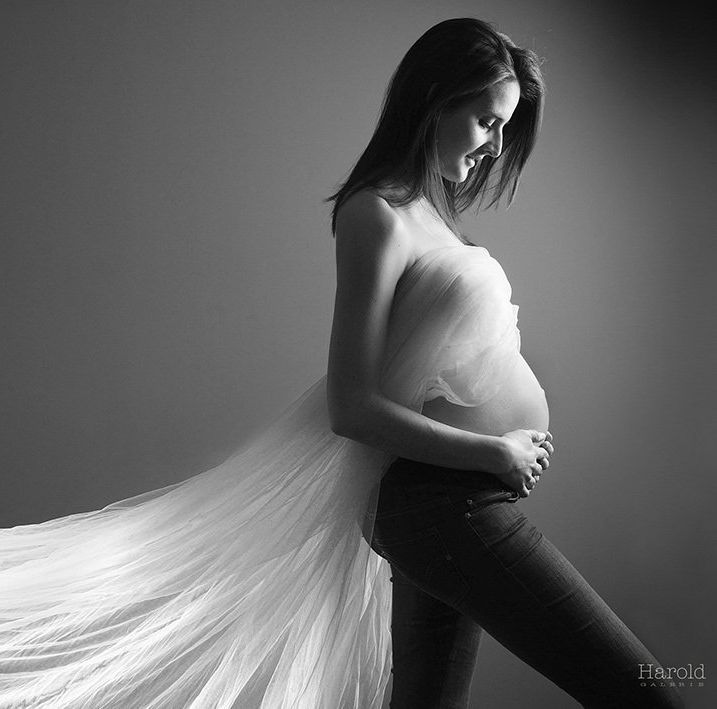 Femme enceinte de profil, mains sur le ventre, avec un tissu fluide et translucide.