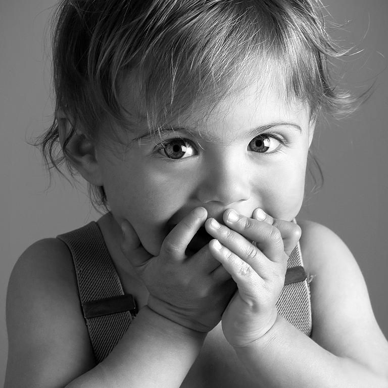 Gros plan sur un enfant se couvrant la bouche des deux mains, regardant l'objectif.