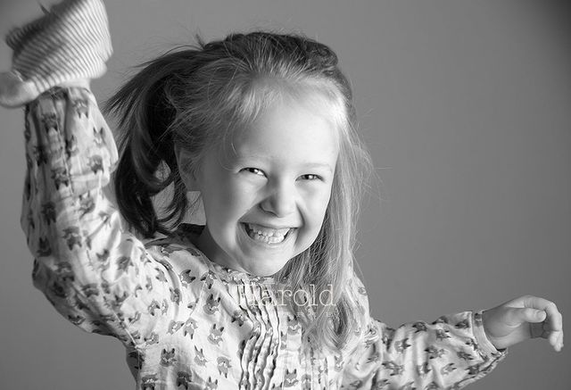 Enfant souriante, les bras levés, vêtue d'une chemise à motifs.