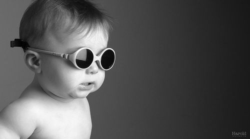 Enfant portant des lunettes de soleil rondes sur fond sombre uni.