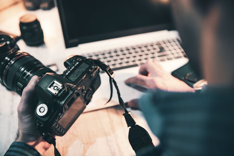 Une personne regarde des photos sur un appareil photo reflex numérique à côté d'un ordinateur portable posé sur un bureau.