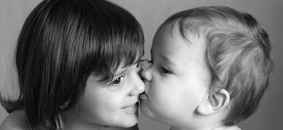 Deux visages en gros plan, nez contre nez, un enfant embrassant un autre, en noir et blanc.