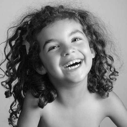 Enfant souriant aux cheveux bouclés, riant sur un fond uni.