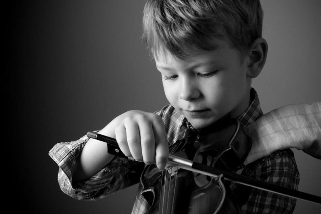 Enfant jouant du violon, concentré sur les cordes, sur une photo en noir et blanc.