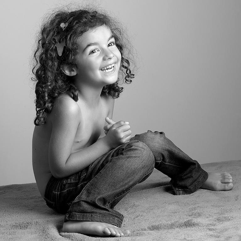 Enfant souriant aux cheveux bouclés assis sur un lit.