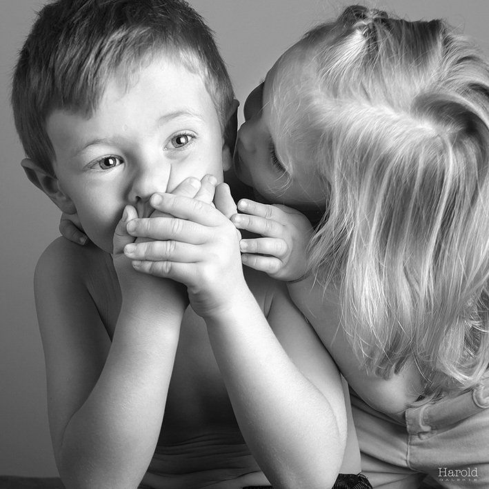 Deux enfants très proches l'un de l'autre ; l'un murmure à l'oreille de l'autre en se couvrant la bouche.