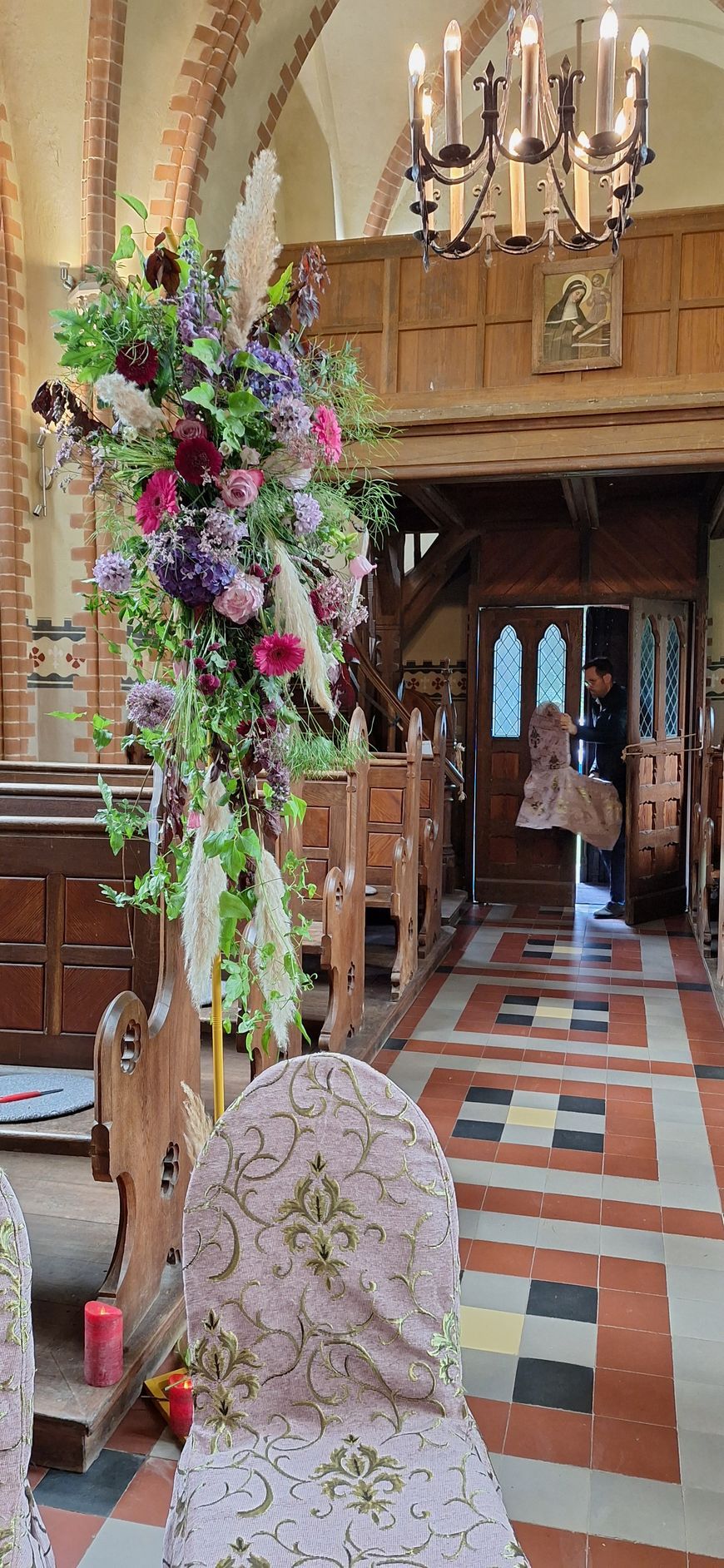 Kirchendekoration mit Blumenarrangement und Kerzen vor Holzbank und Altarbereich