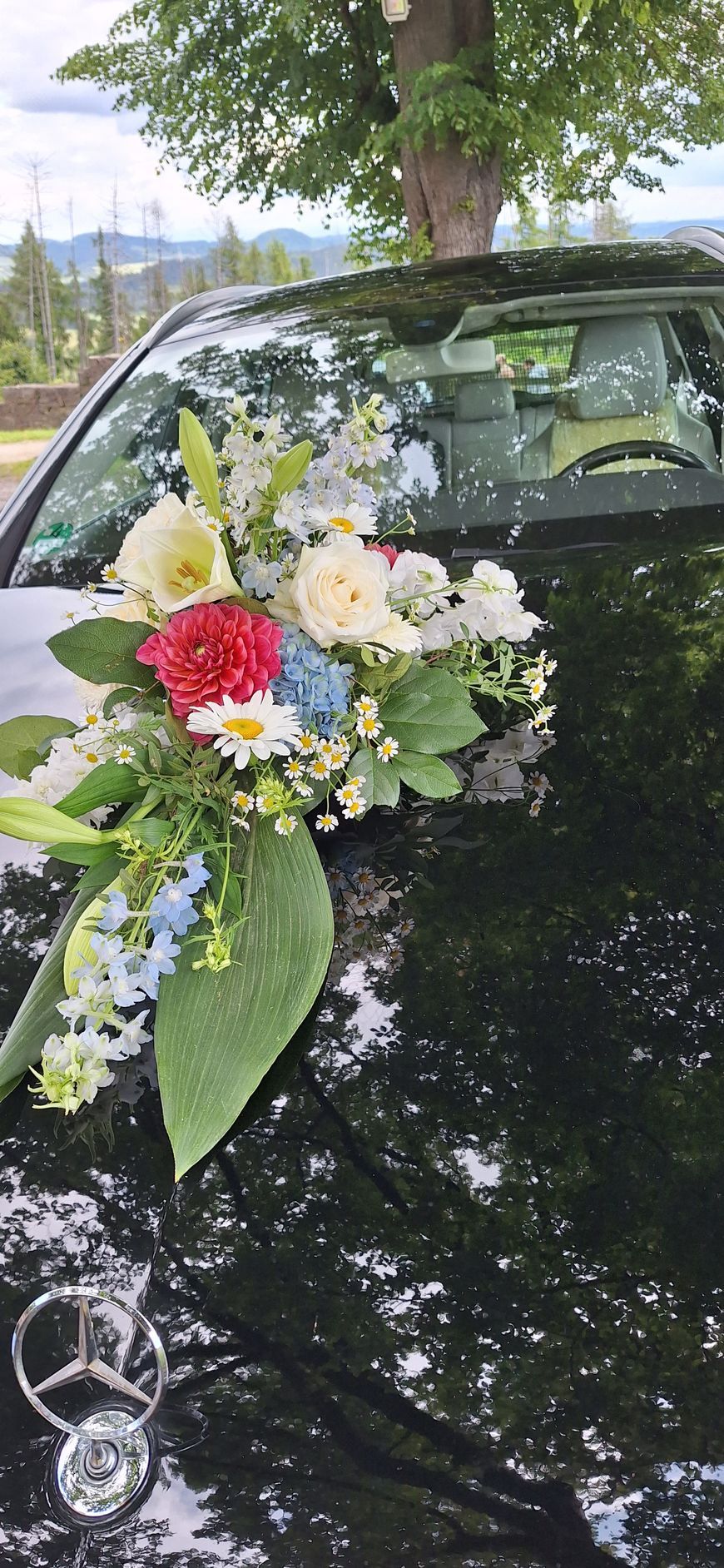 Auto unter Baum mit Aussicht und Blumengesteck darauf.
