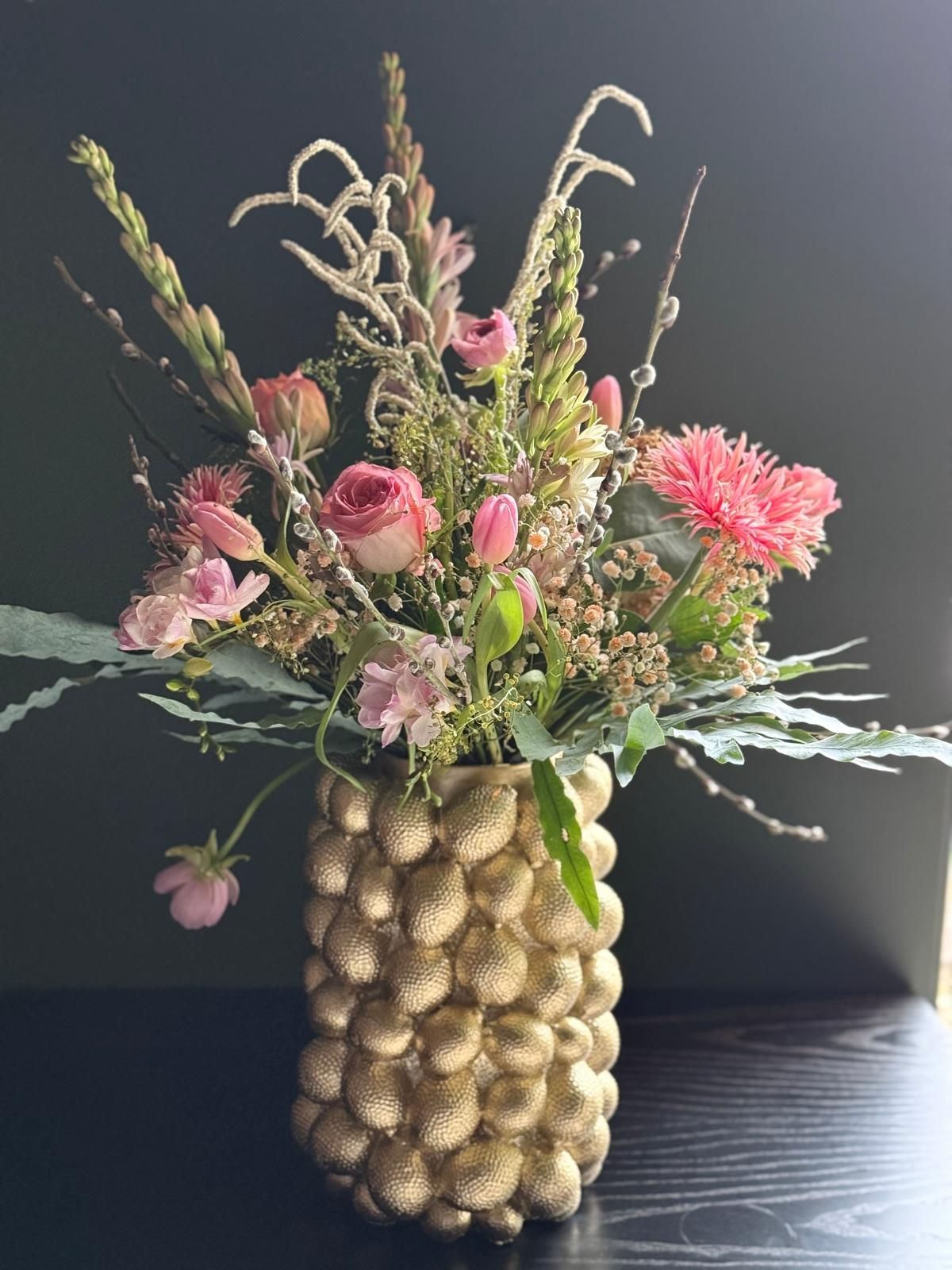 Festliche Blumendekoration mit rosa Blüten und Gräsern in eleganter goldener Vase