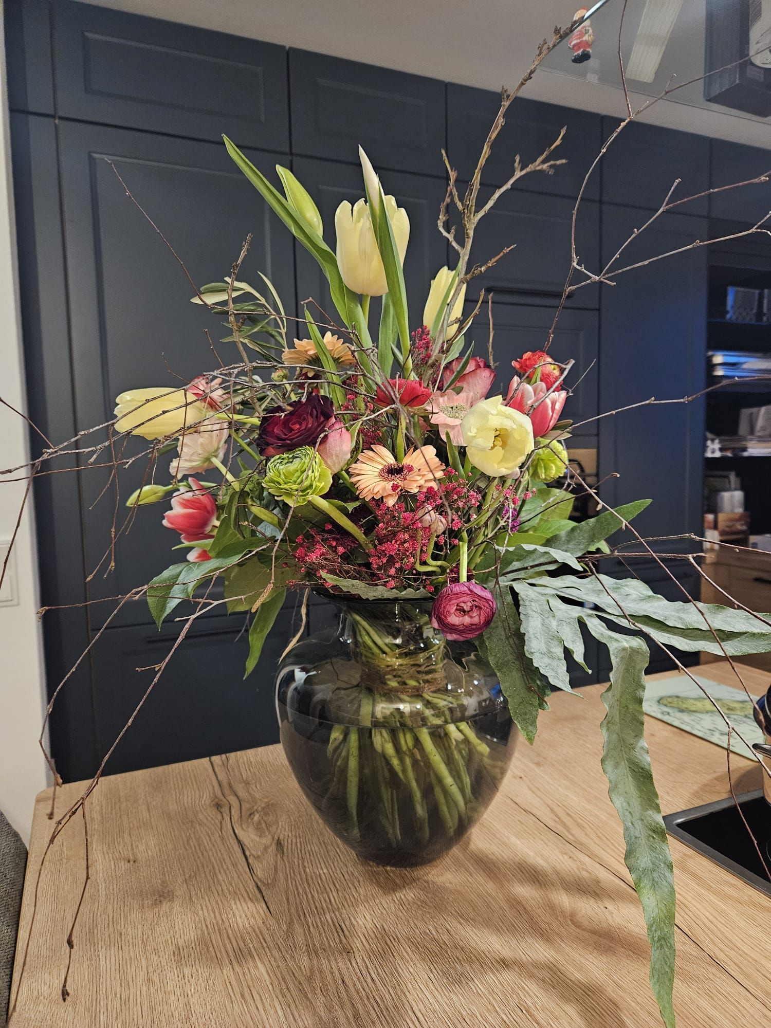 Modernes Blumenarrangement mit Tulpen, Rosen und Zweigen in Glasvase