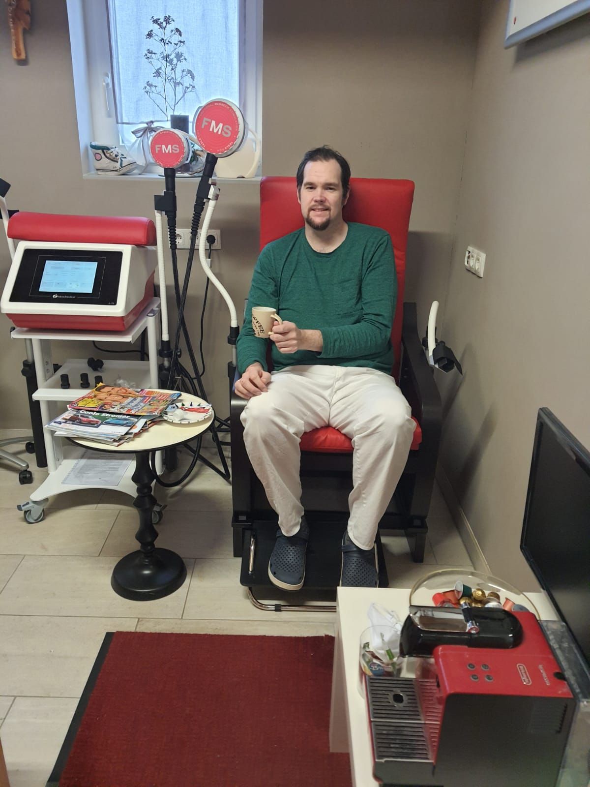 Ein Mann sitzt in einem Raum auf einem Stuhl und hält eine Tasse Kaffee in der Hand.