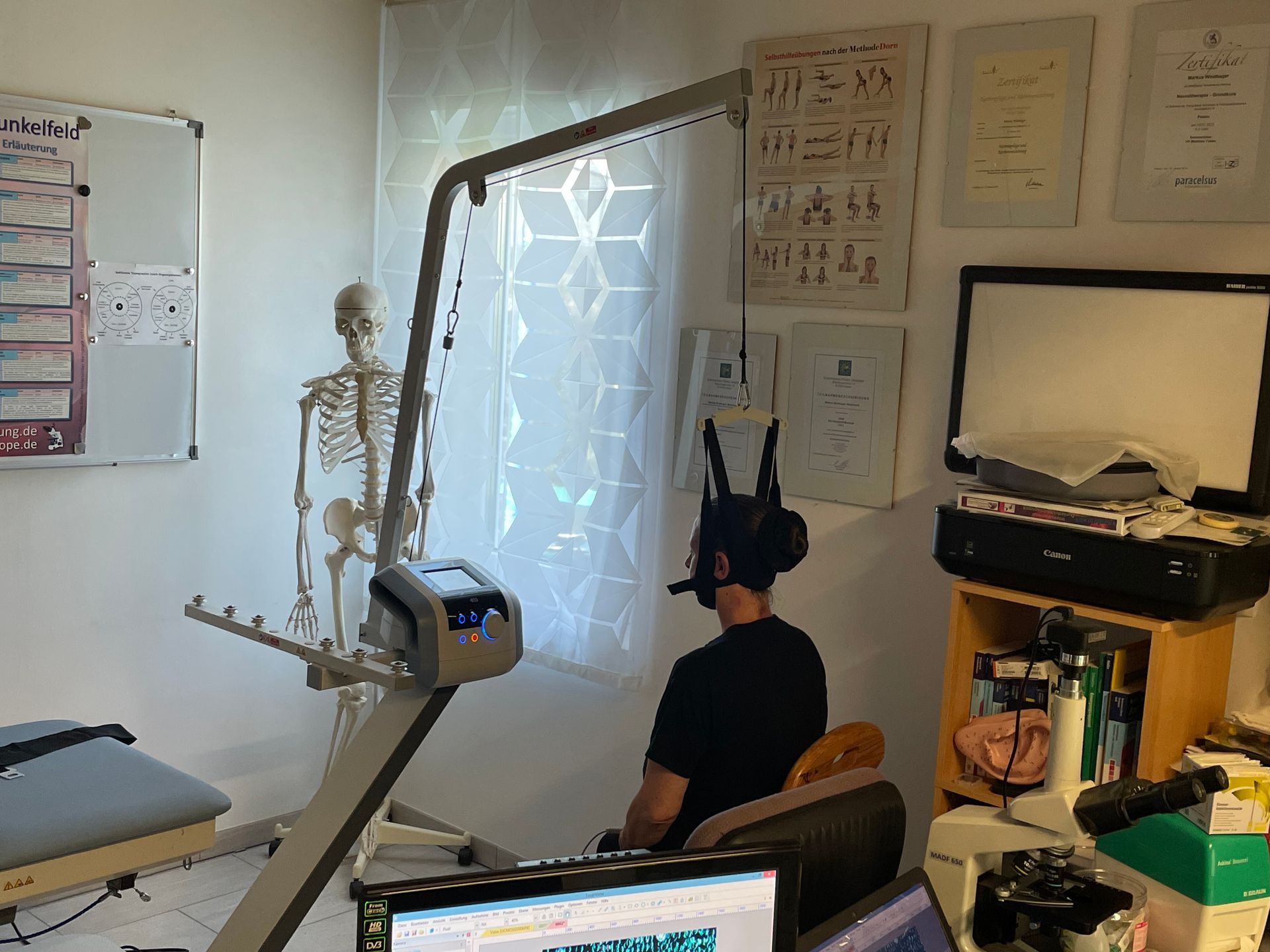 Ein Mann sitzt in einem Raum vor einem Computer, im Hintergrund ist ein Skelett zu sehen.