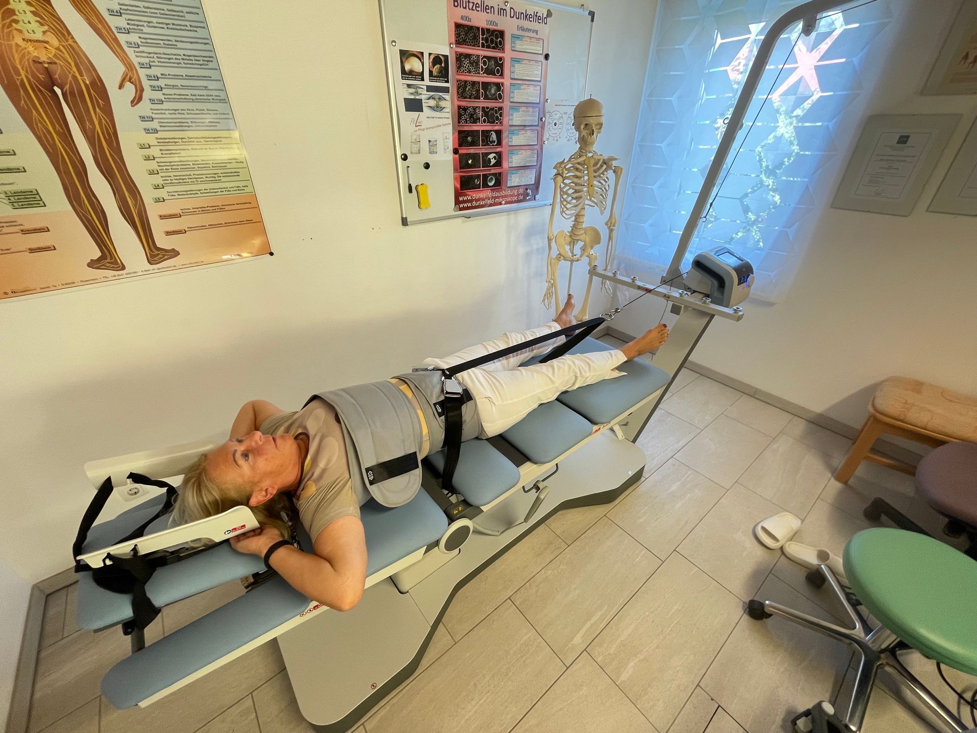 Eine Frau liegt auf einer Trage in einem Raum. Im Hintergrund ist ein Skelett zu sehen.