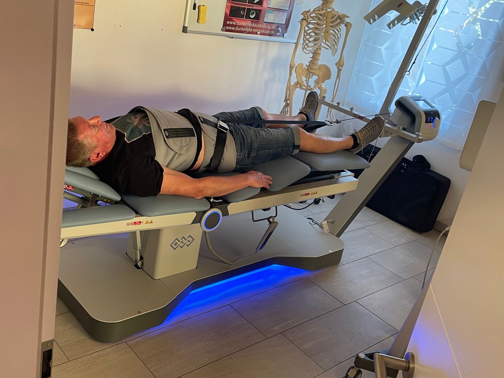 Ein Mann liegt auf einer Trage in einem Raum. Im Hintergrund ist ein Skelett zu sehen.