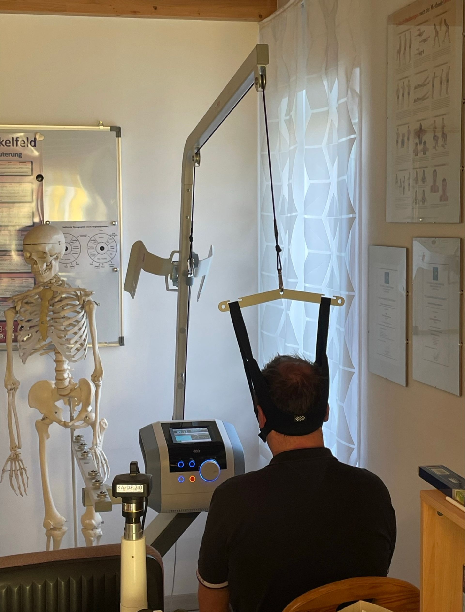 Ein Mann sitzt vor einer Maschine, im Hintergrund ist ein Skelett zu sehen.