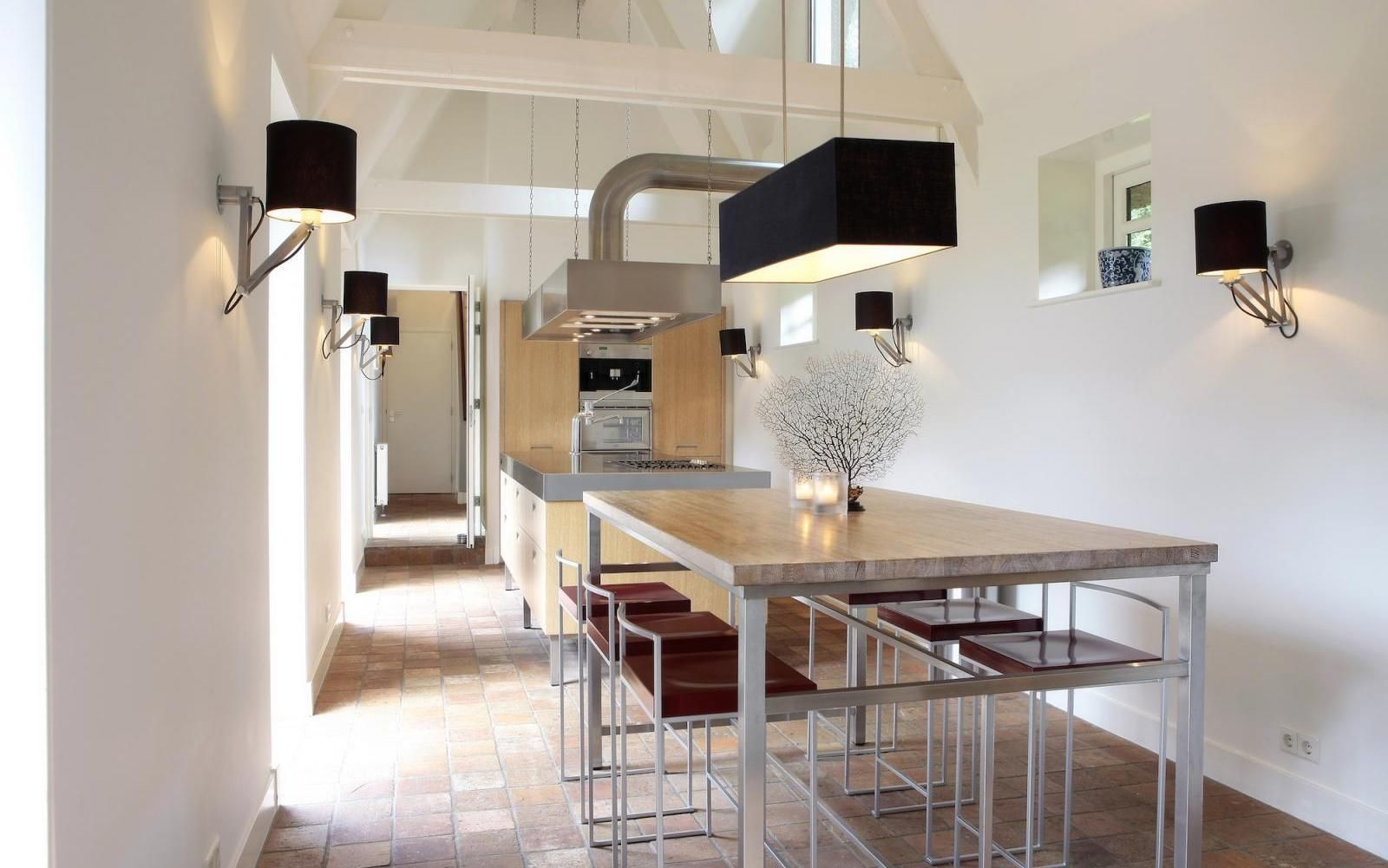 Een moderne, lichte keuken met een houten kookeiland, barkrukken, zwarte hanglampen en wandlampen.