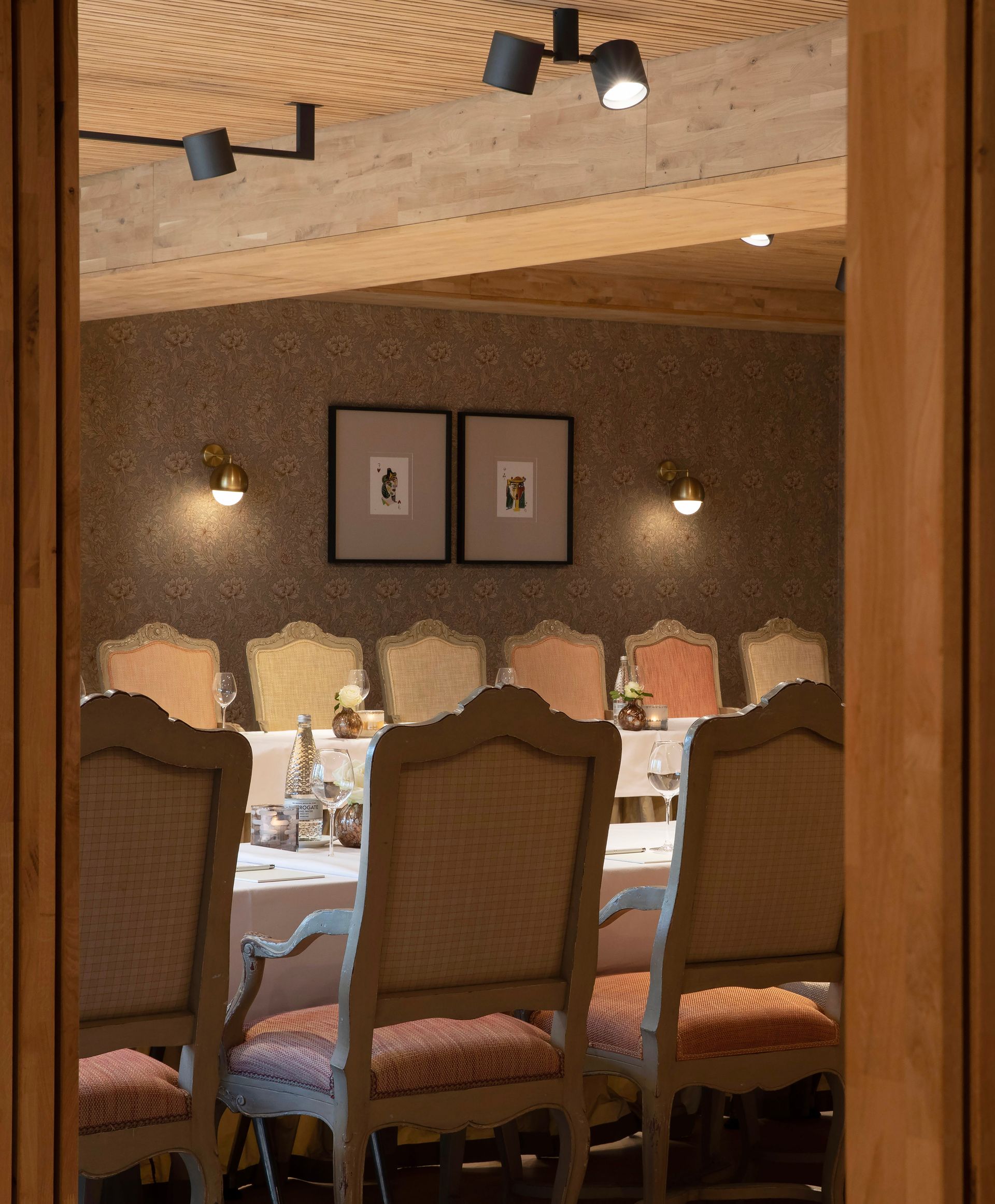 Een eetkamer met een lange tafel, elegante gestoffeerde stoelen en warme, sfeervolle verlichting die door een houten frame heen schijnt.