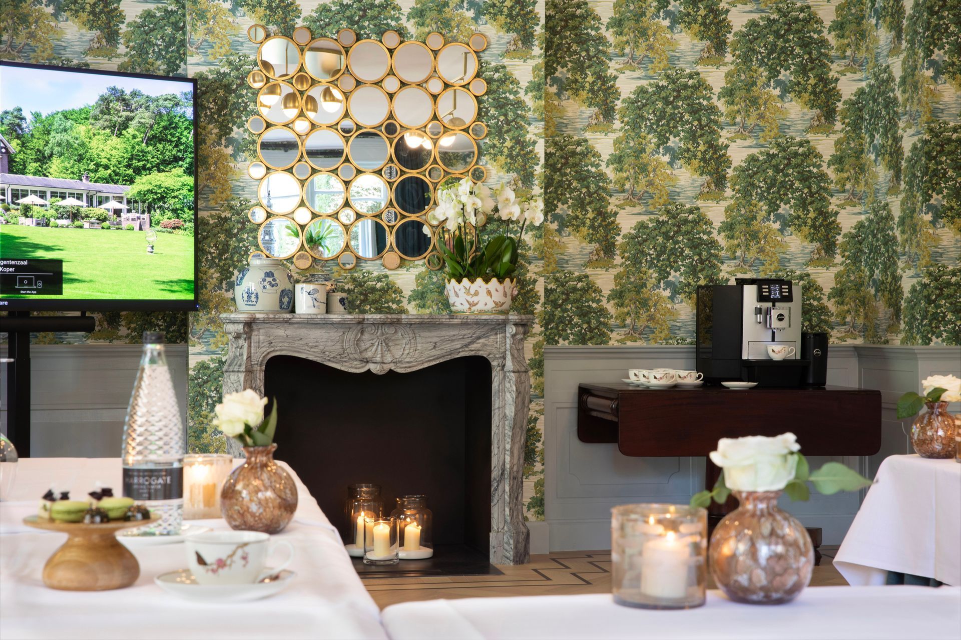 Een weelderige tuin met een kronkelend grindpad, een groen gazon, keurig gesnoeide hagen en een bloeiende boom, omgeven door hoge bosbomen.