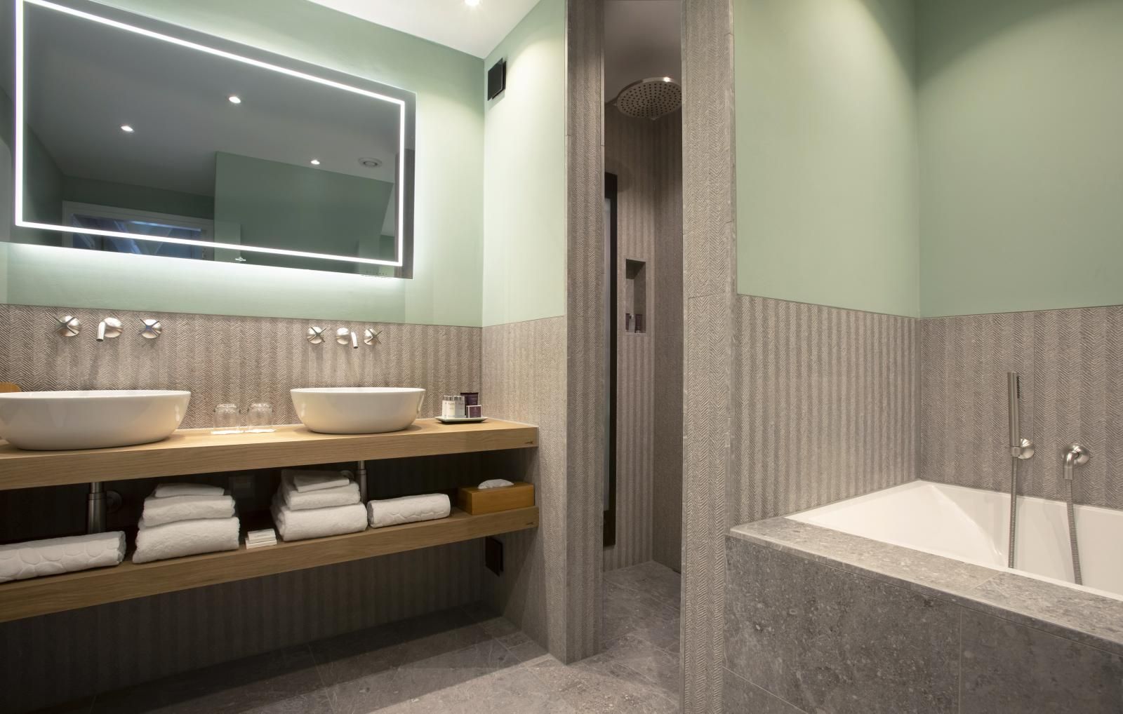 Modernes Badezimmer mit Doppelwaschbecken, beleuchtetem Spiegel und Badewanne in einer separaten, gefliesten Kabine.