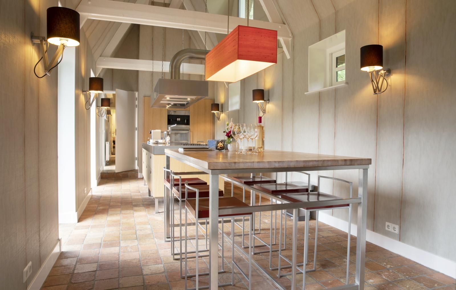 Eine Küche im rustikalen Stil mit einem langen Holztisch, Barhockern und warmem Licht unter einer gewölbten Balkendecke.