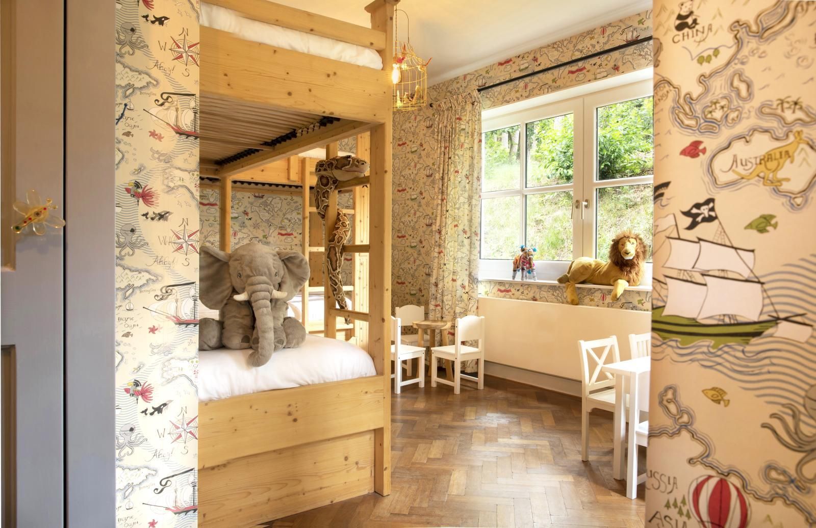 Ein Schlafzimmer mit einem hölzernen Etagenbett, einem Elefanten-Plüschtier, einer Tapete mit Piratenmotiven und kleinen Kindermöbeln.