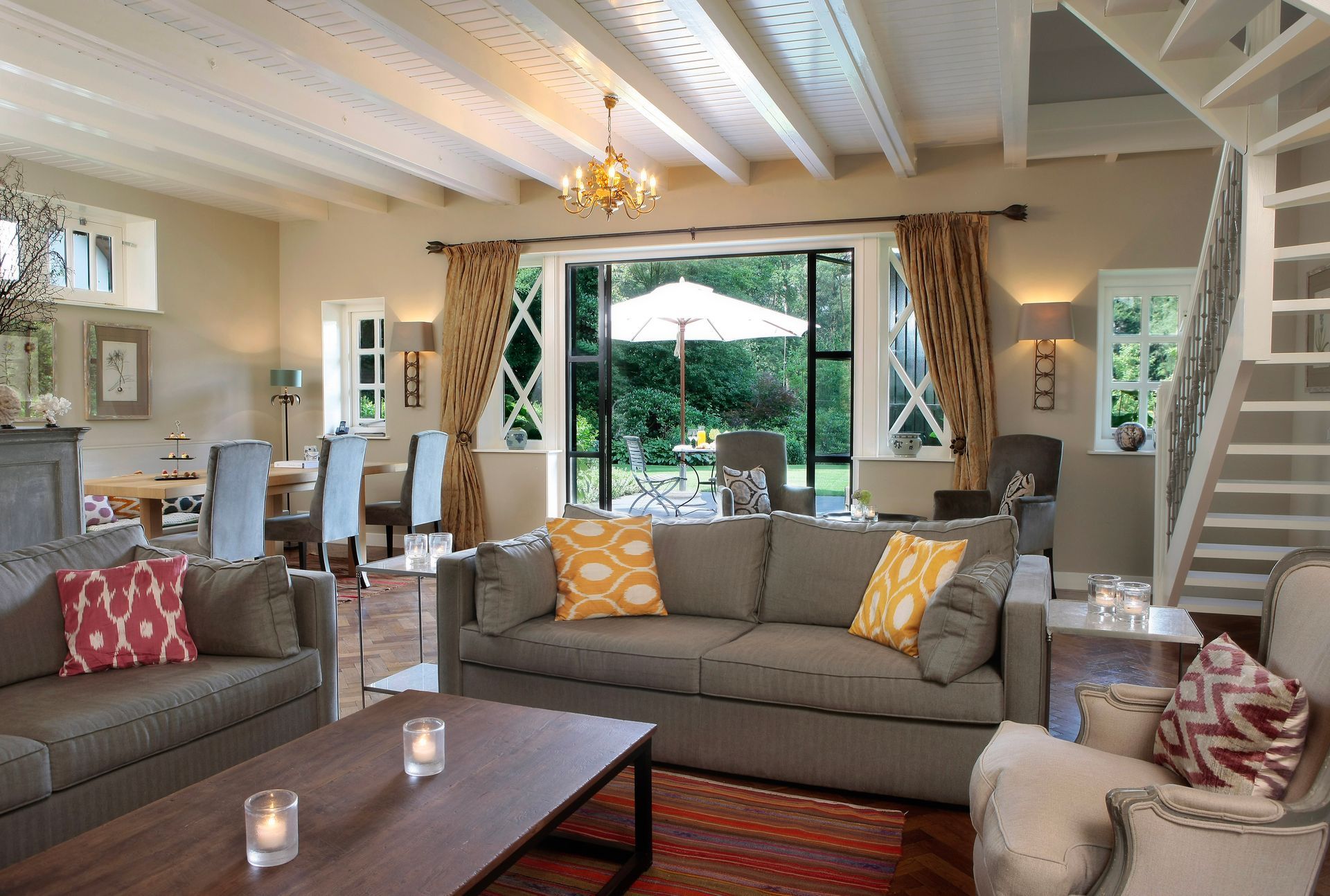 Paarse blauweregenbloemen hangen over een boog die een zonnig terras omlijst, met tafels, stoelen en witte parasols.