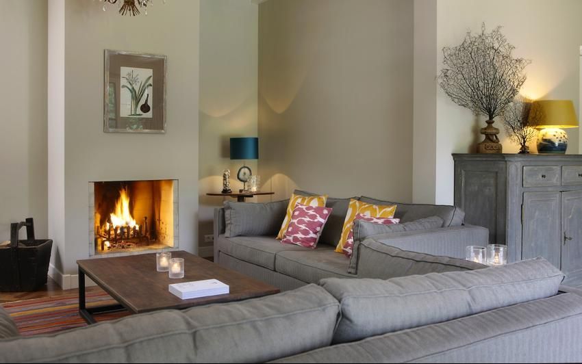 Ein gemütliches Wohnzimmer mit Kamin, grauem Ecksofa, Couchtisch aus Holz und dekorativen Akzenten in einem neutralen Raum.