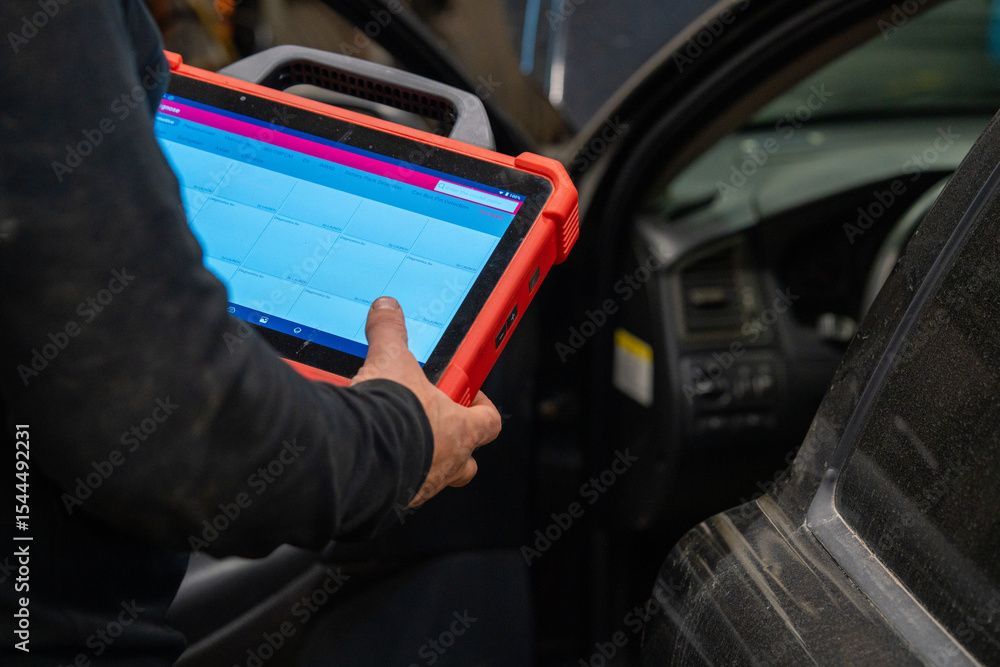Mechaniker benutzt Diagnose-Tablet im Auto; orangefarbenes Gehäuse, blauer Bildschirm.