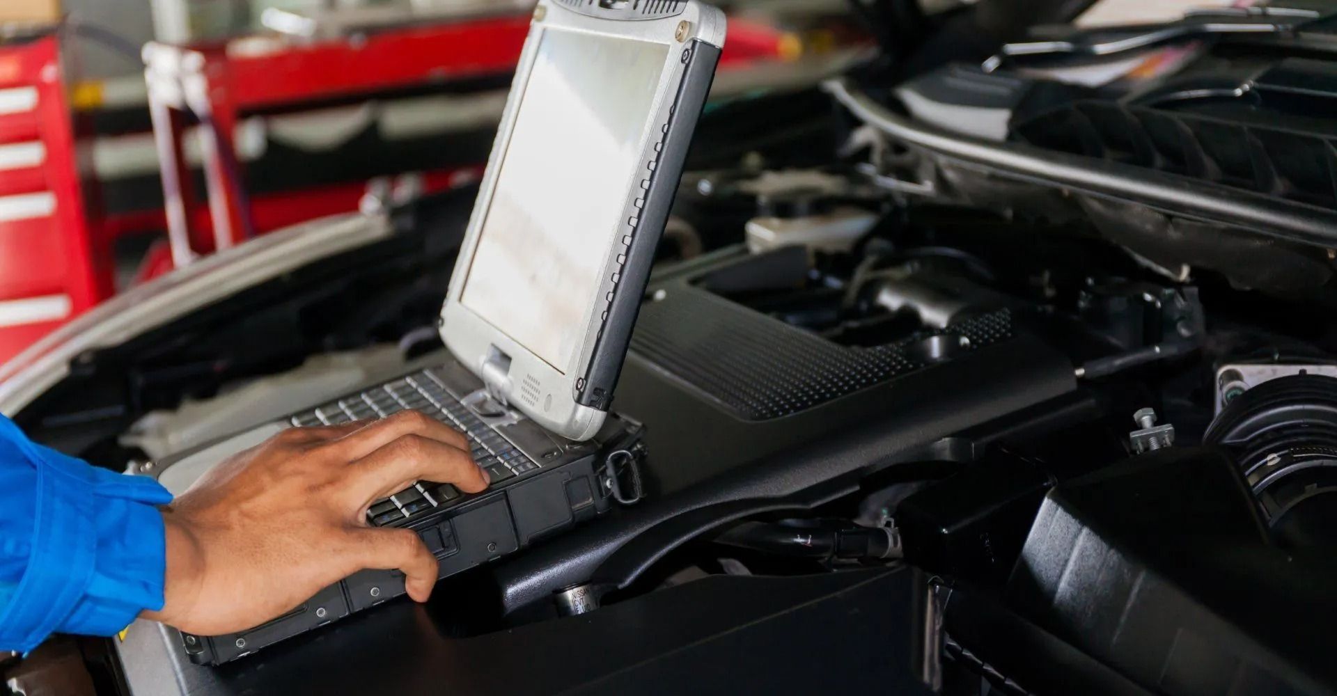 Ein Mechaniker benutzt in einer Autowerkstatt ein Laptop-Diagnosegerät an einem Automotor.