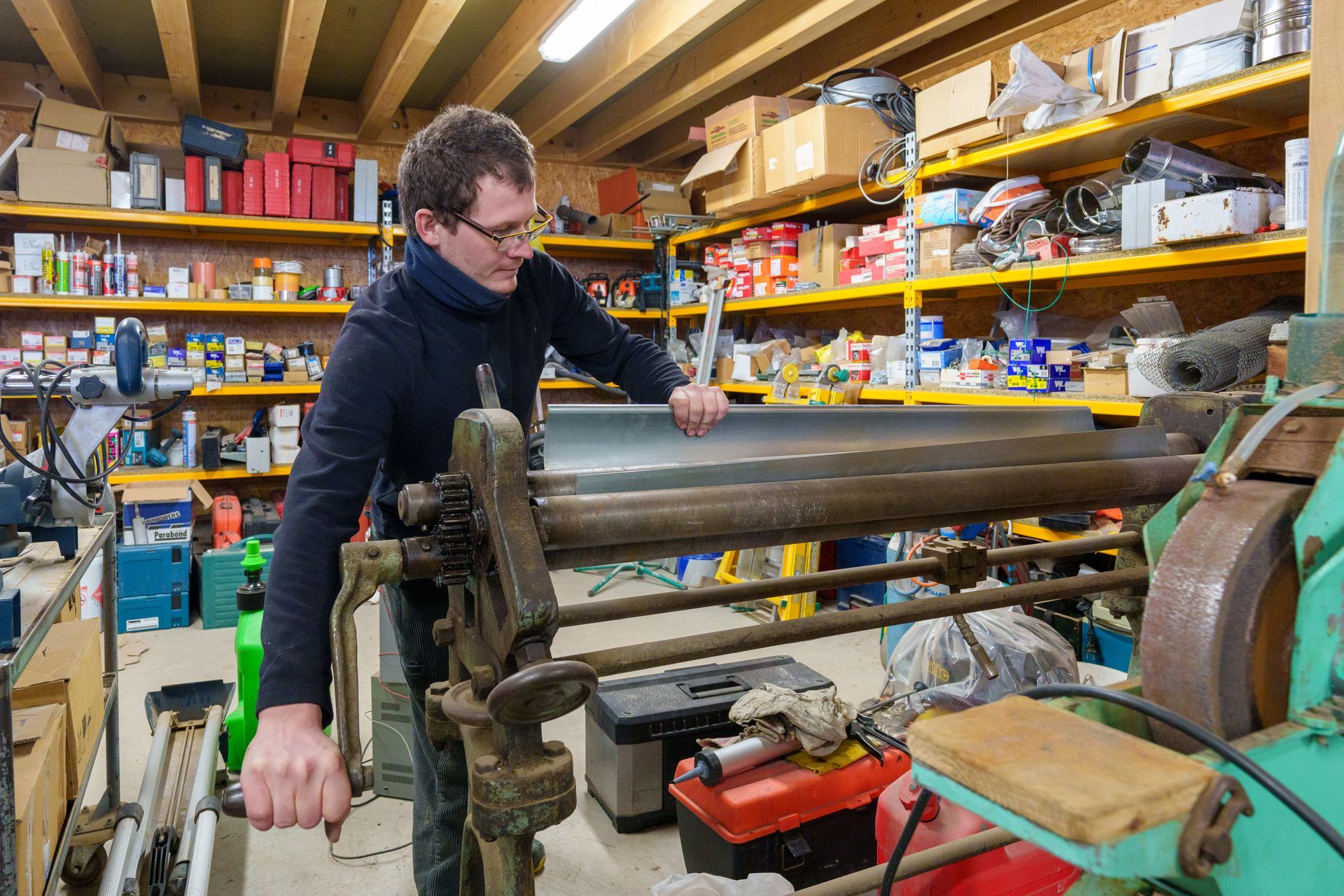 Une personne travaille sur une grande machine métallique dans un atelier encombré d'étagères remplies de fournitures.