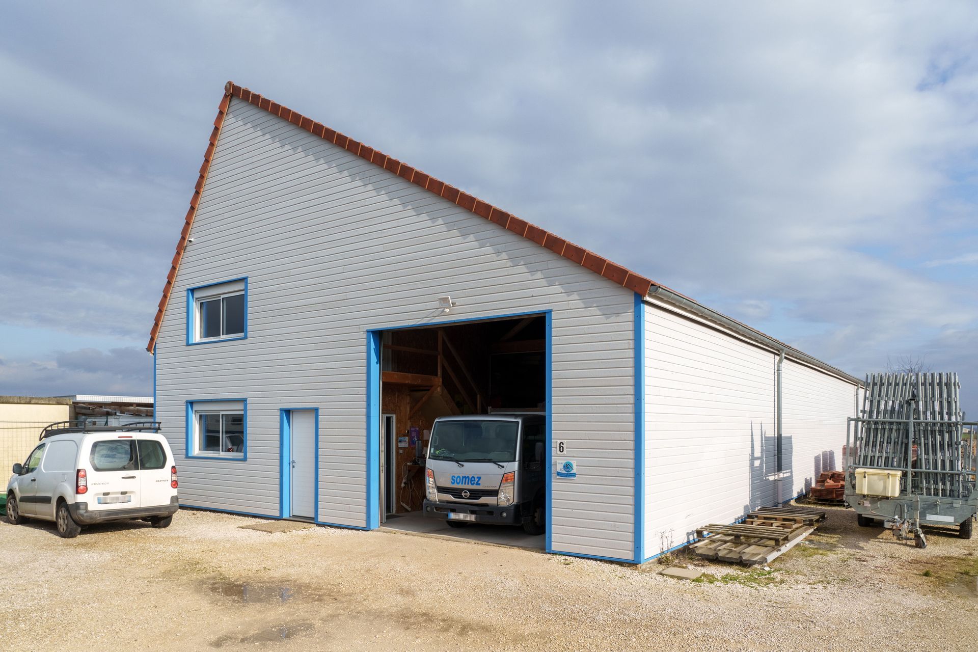 Maison construite avec garage, fourgonnette blanche à l'intérieur et un autre véhicule garé à l'extérieur.