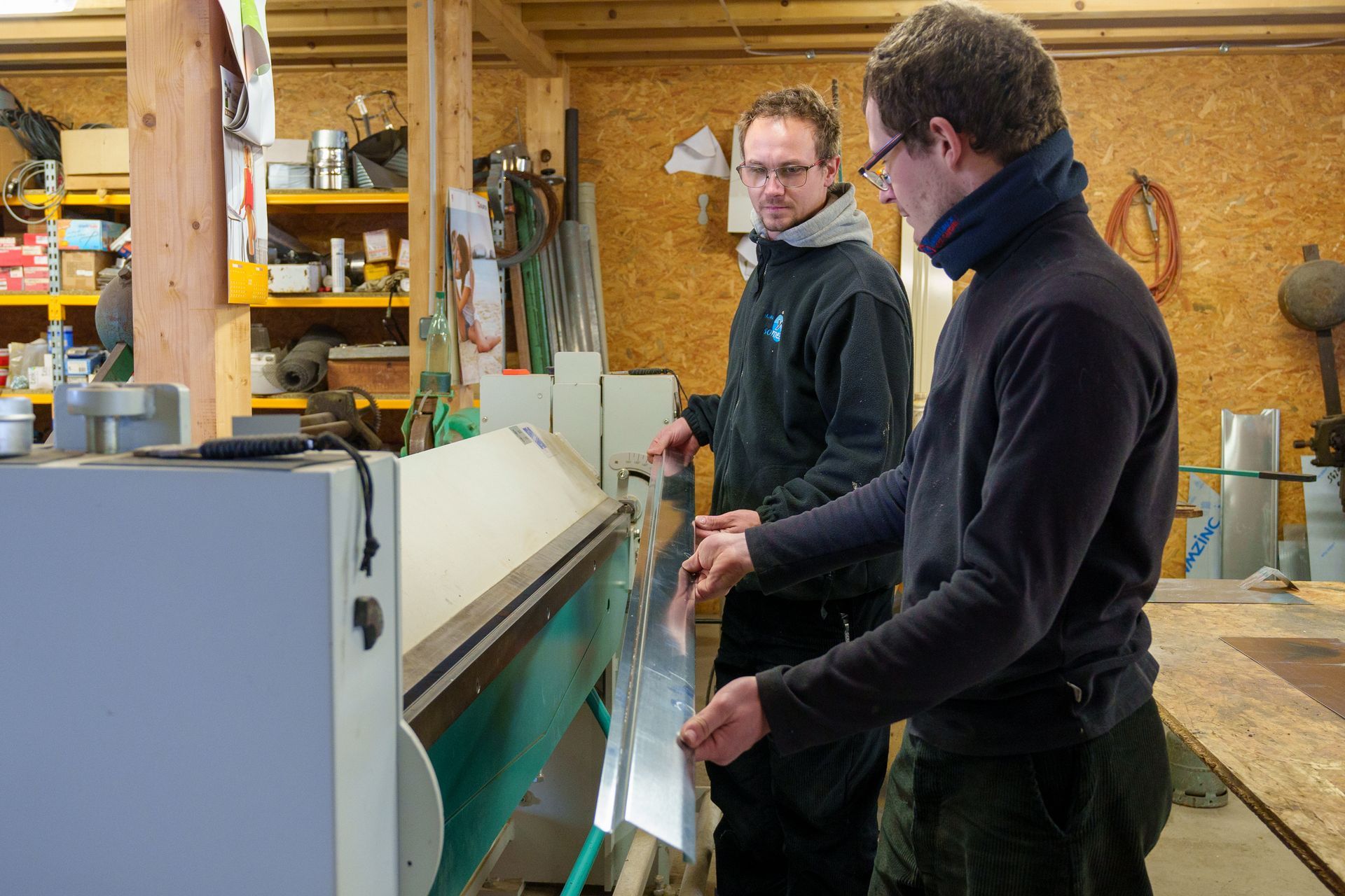 Deux personnes examinent une grande machine dans un atelier, près d'étagères et d'outils.