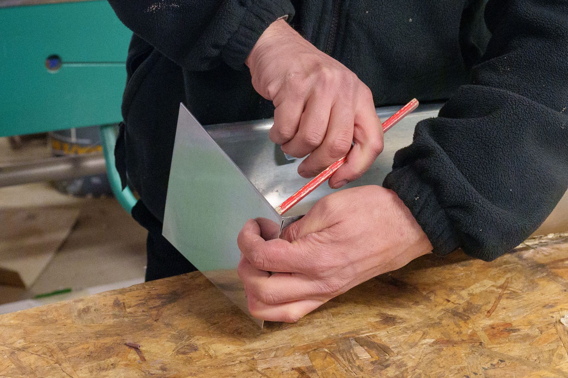 Des mains mesurent une feuille grise avec un crayon sur un établi.
