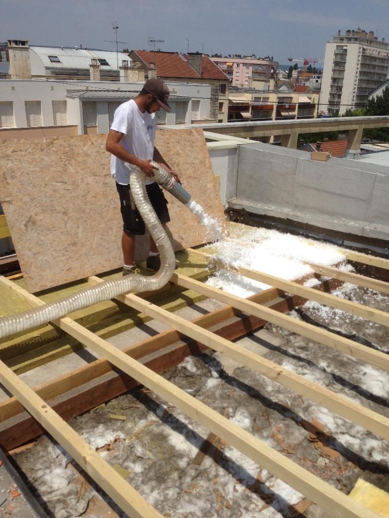 Une personne verse de la mousse isolante liquide sur une charpente de toit en construction