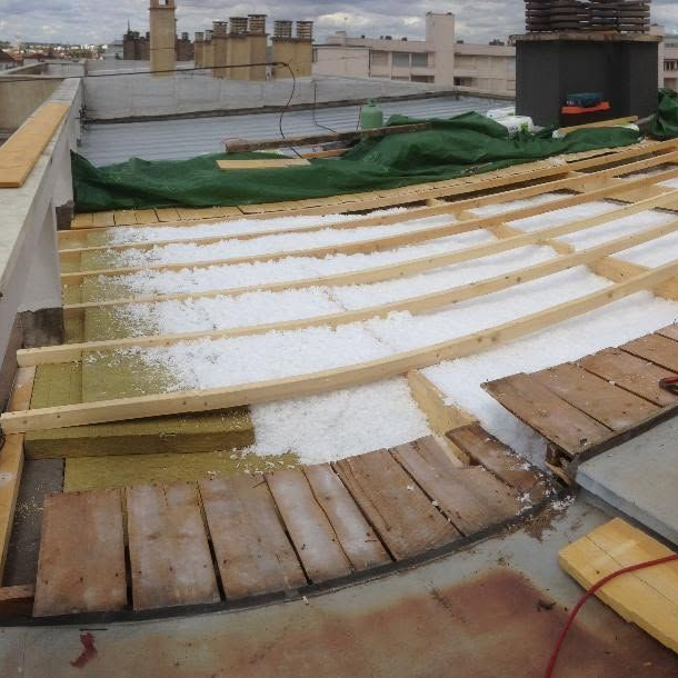 Toiture en construction avec des planches de bois, recouverte de neige et une bâche verte près des cheminées.