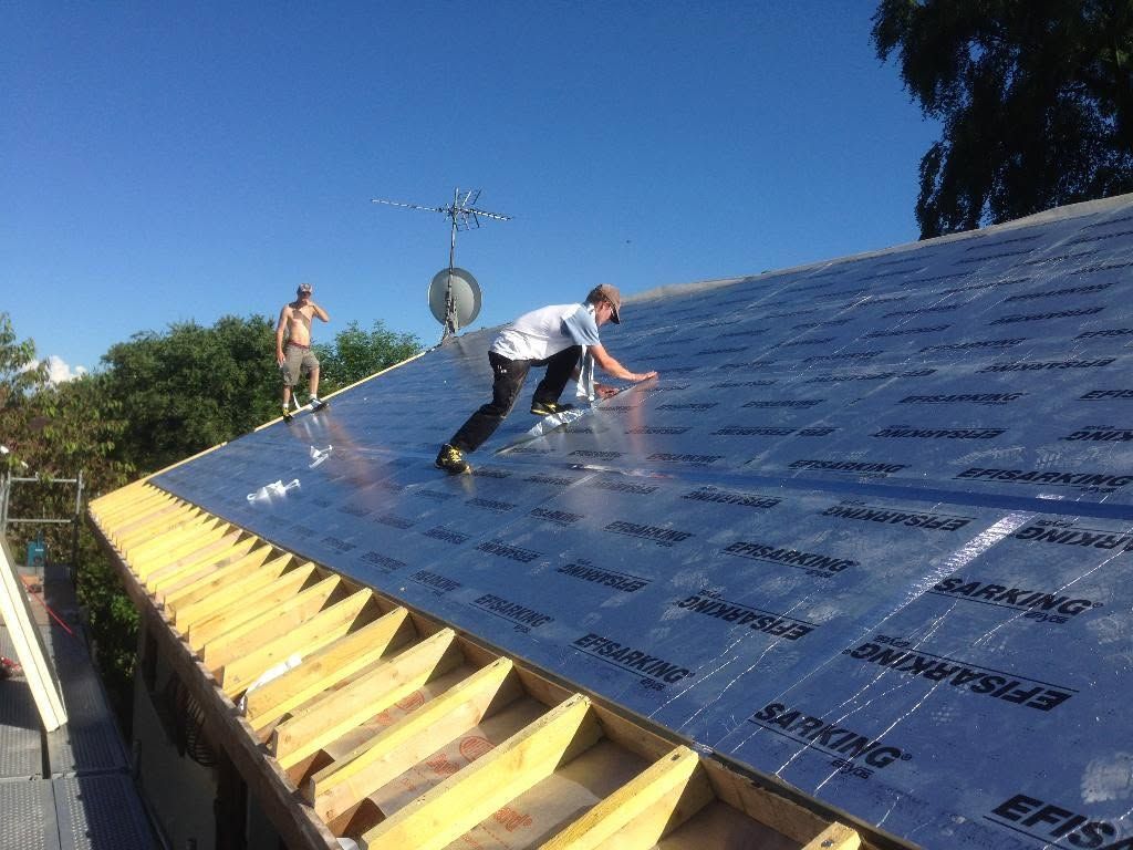 Des ouvriers installent uneisolation de toiture sur un toit en pente sous un ciel bleu dégagé.
