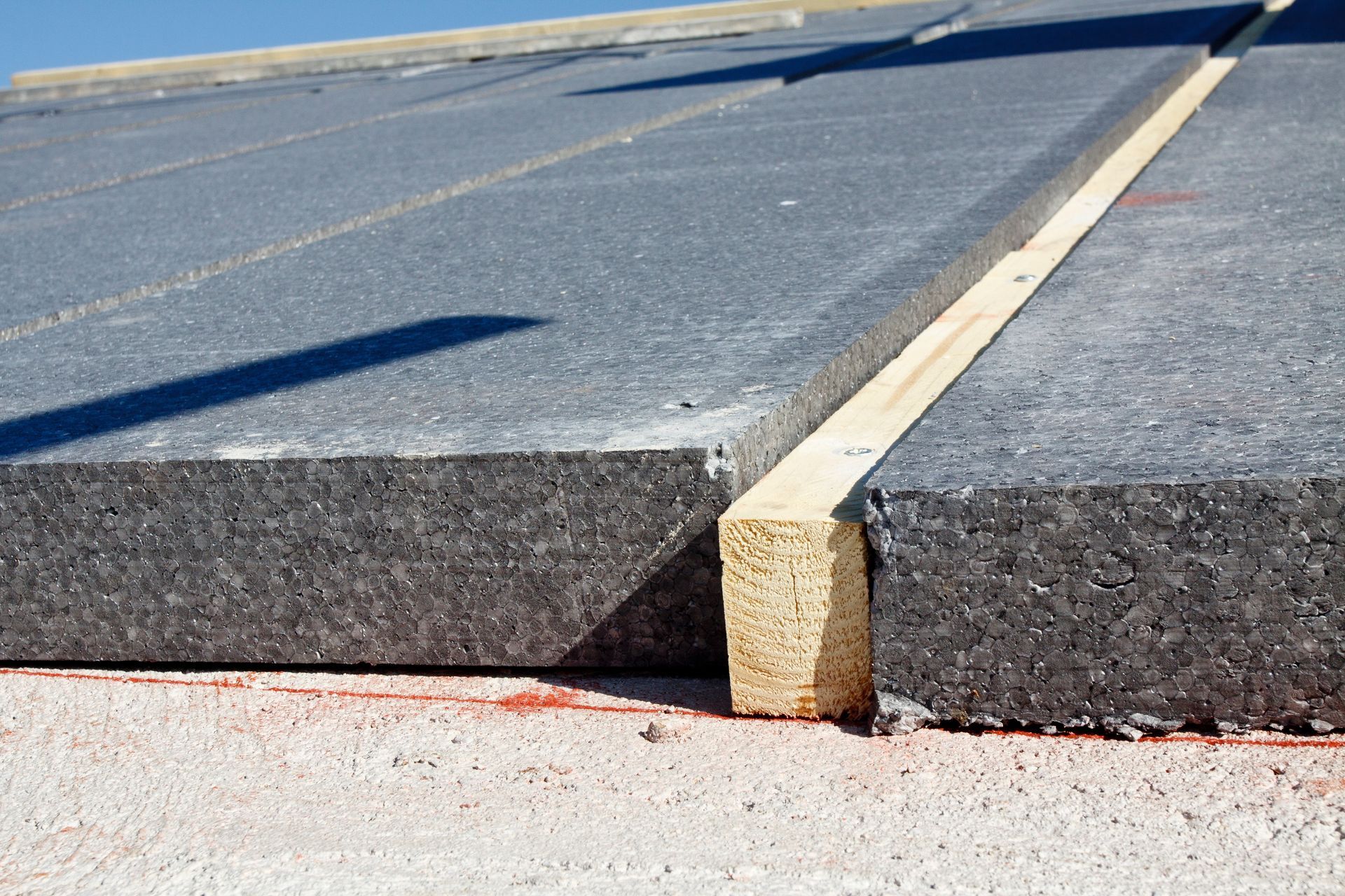 Gros plan sur une route asphaltée fissurée avec un joint en béton surélevé et une ligne centrale jaune.
