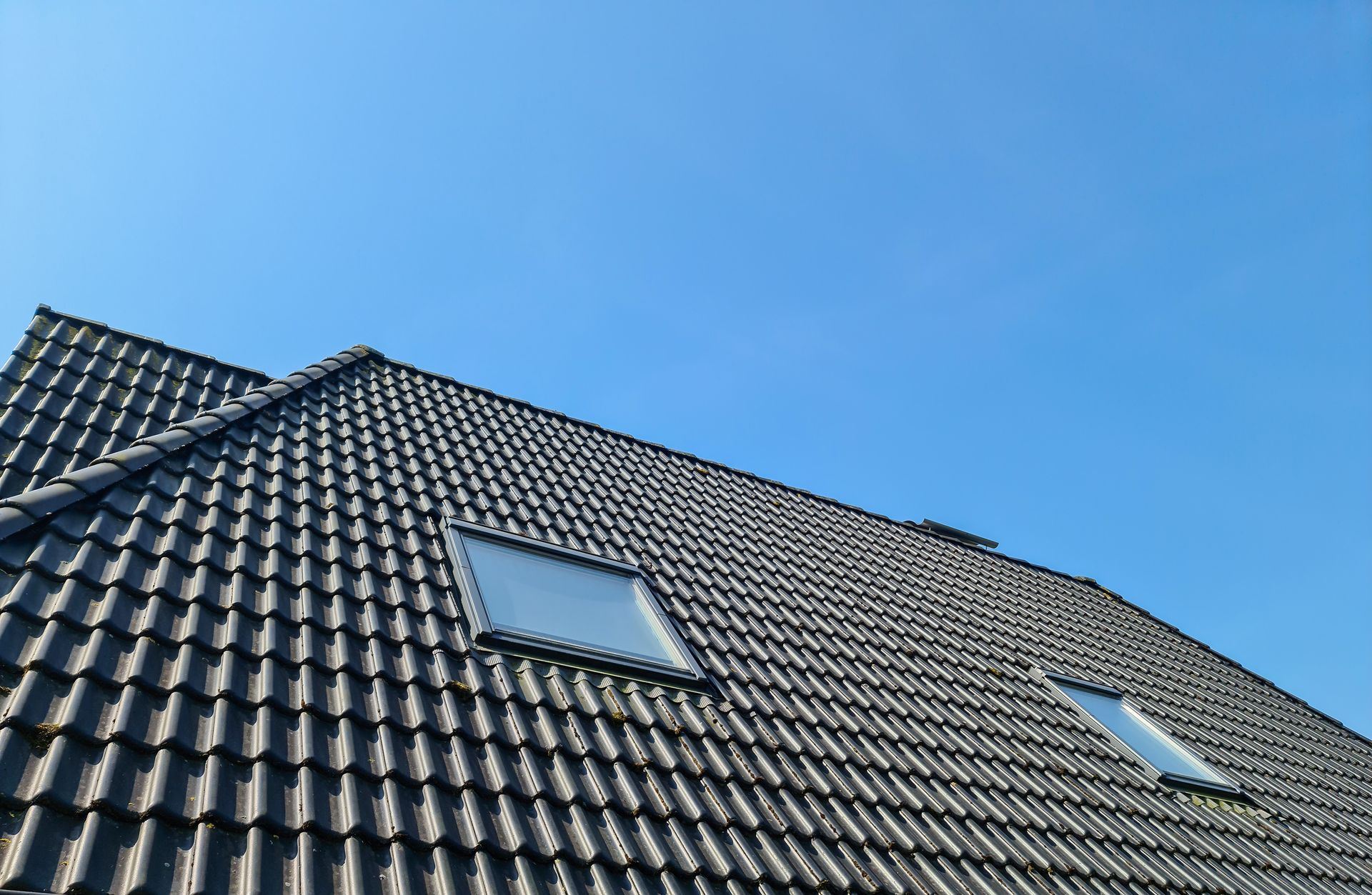 Toit de tuiles avec deux puits de lumière sur un ciel bleu clair.