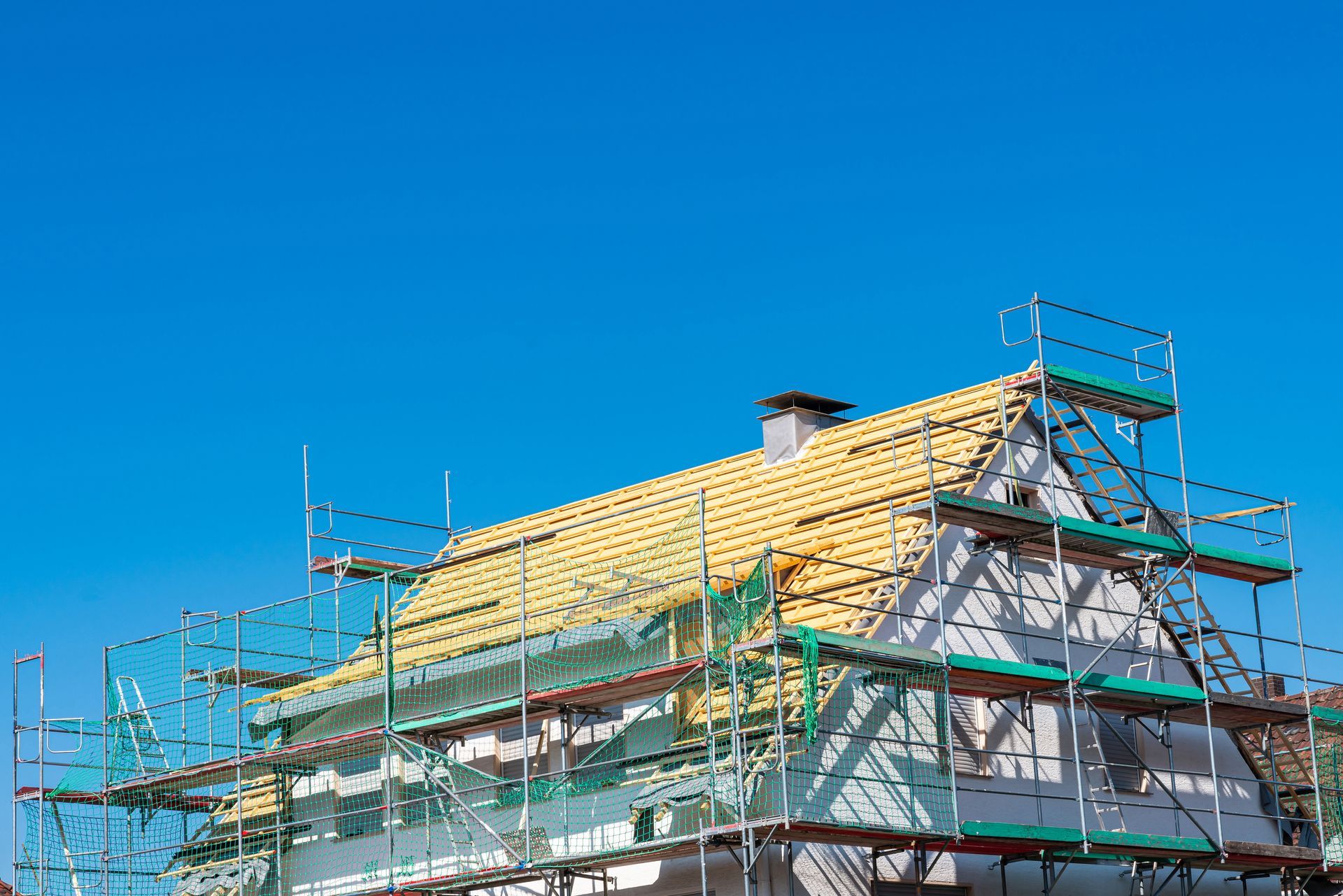 Toiture de maison en construction avec échafaudages verts sur fond de ciel bleu