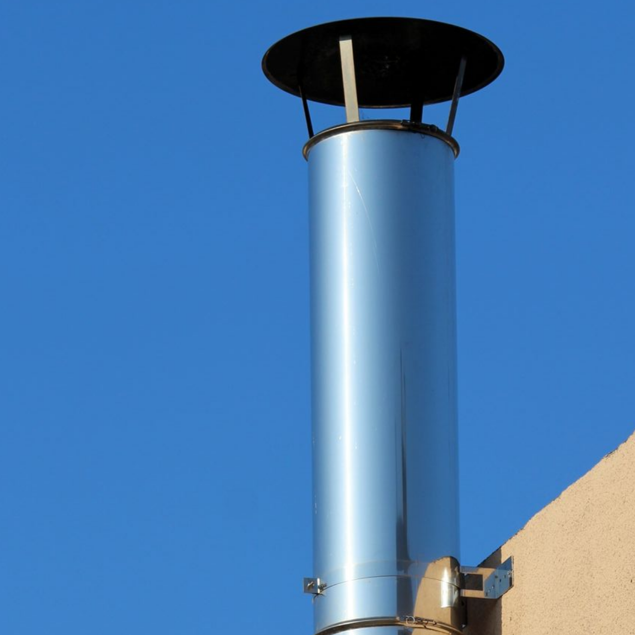 Cheminée argentée sur le toit se détachant sur un ciel bleu clair, à côté d'un mur beige.