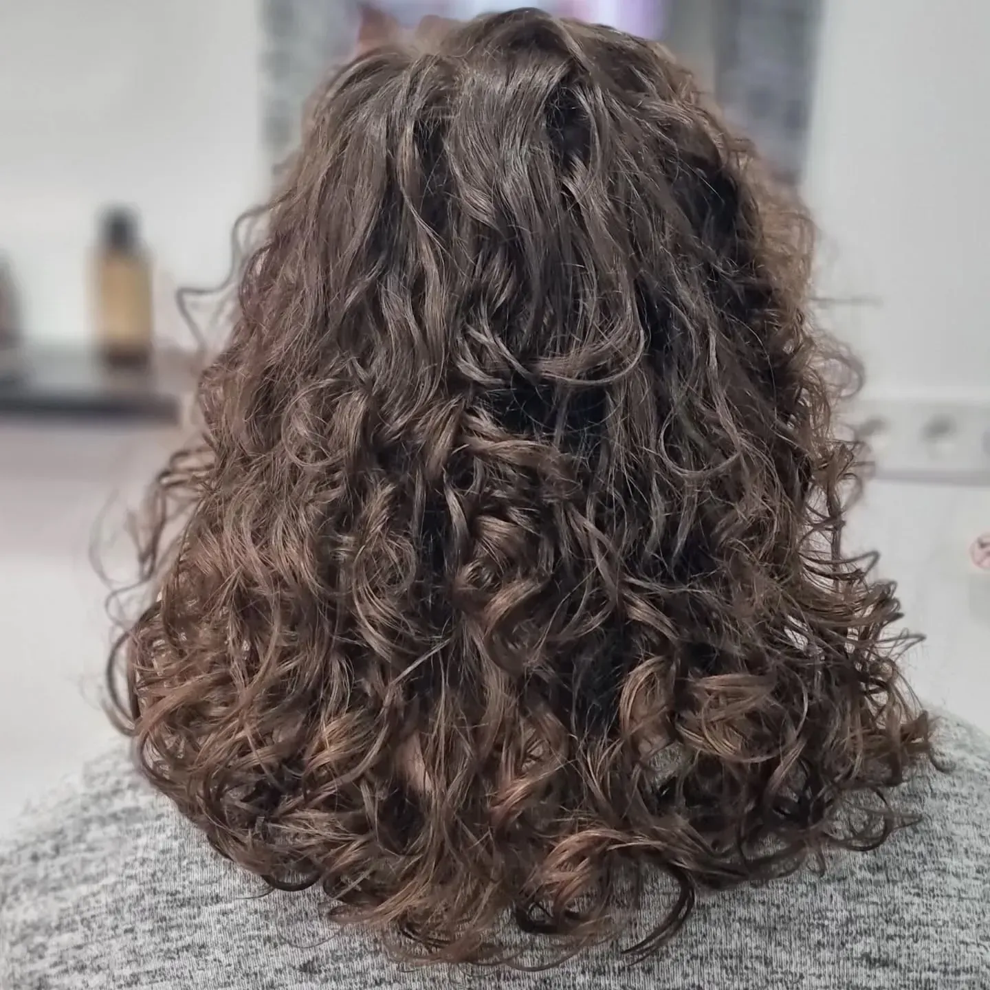 Vista posterior de una persona con cabello rizado de color castaño oscuro y longitud media.