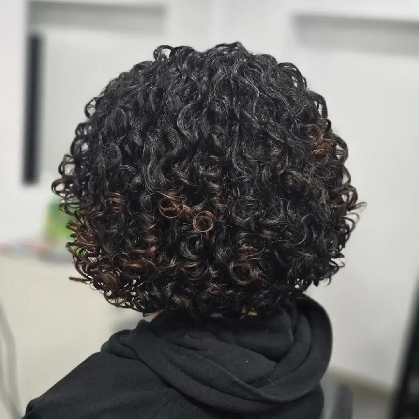 Vista desde atrás de una melena corta, voluminosa y oscura, rizada, con reflejos castaños cálidos.