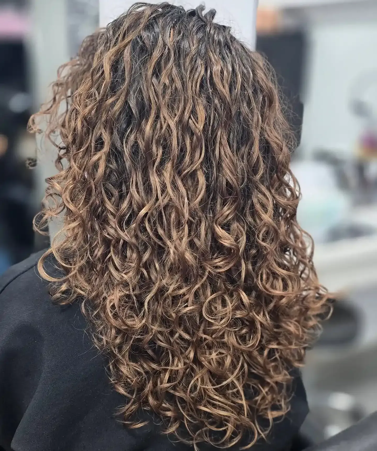 Vista posterior de una larga melena castaña, ondulada y capeada, con reflejos color caramelo, peinada en rizos sueltos.