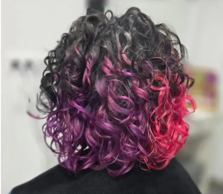 Vista posterior del cabello rizado, cuyas raíces se transforman en puntas moradas y de color rosa brillante.