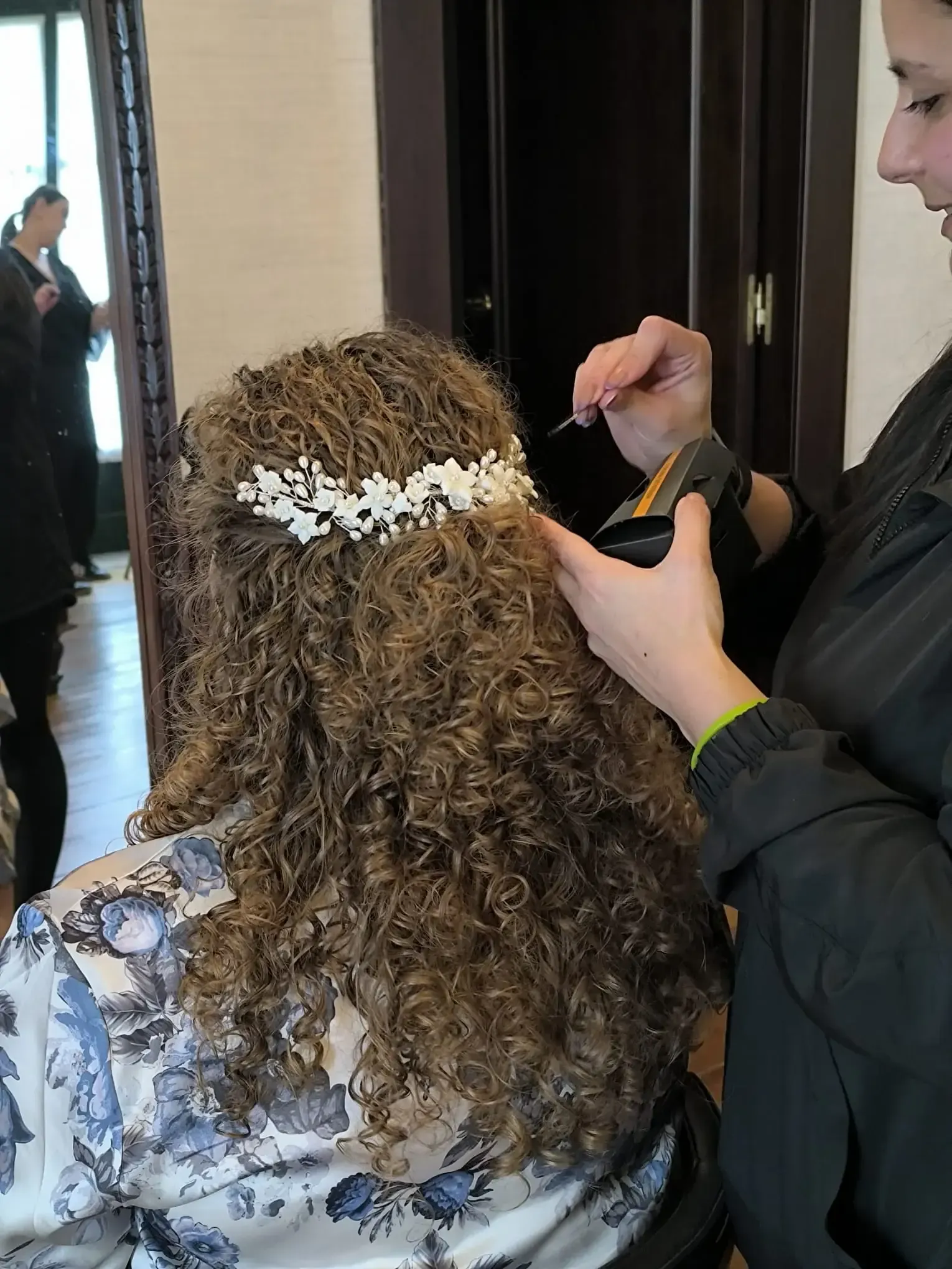 Un peinado recogido bajo y texturizado con un detalle floral decorativo de follaje y pequeñas flores moradas y blancas.