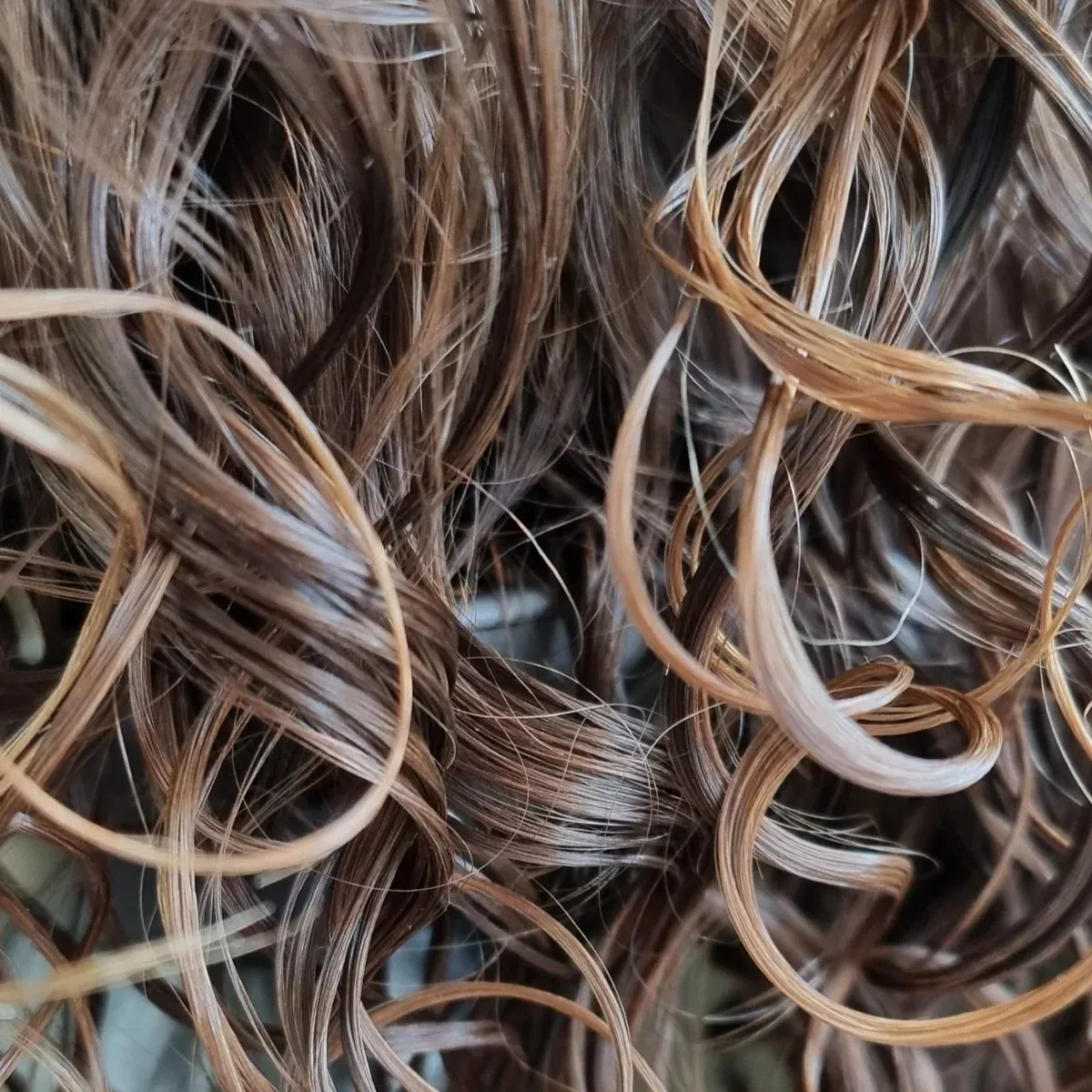 Primer plano de una melena castaña, ondulada y con textura, iluminada por una suave luz natural dorada.