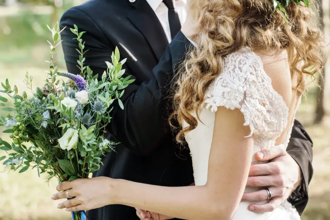 Un peinado recogido bajo y texturizado con un detalle floral decorativo de follaje y pequeñas flores moradas y blancas.