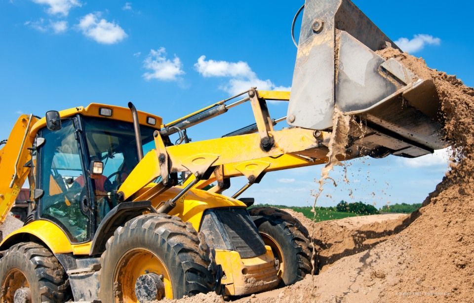 Ein gelber Baggerlader gräbt Sand auf einer Baustelle unter blauem Himmel